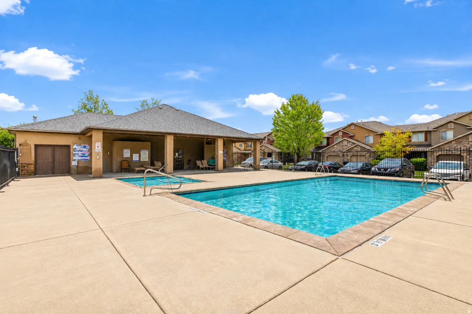 Community swimming pool with crystal-clear water, spacious concrete decking, and an adjoining clubhouse featuring multiple garage bays and covered pavilion areas