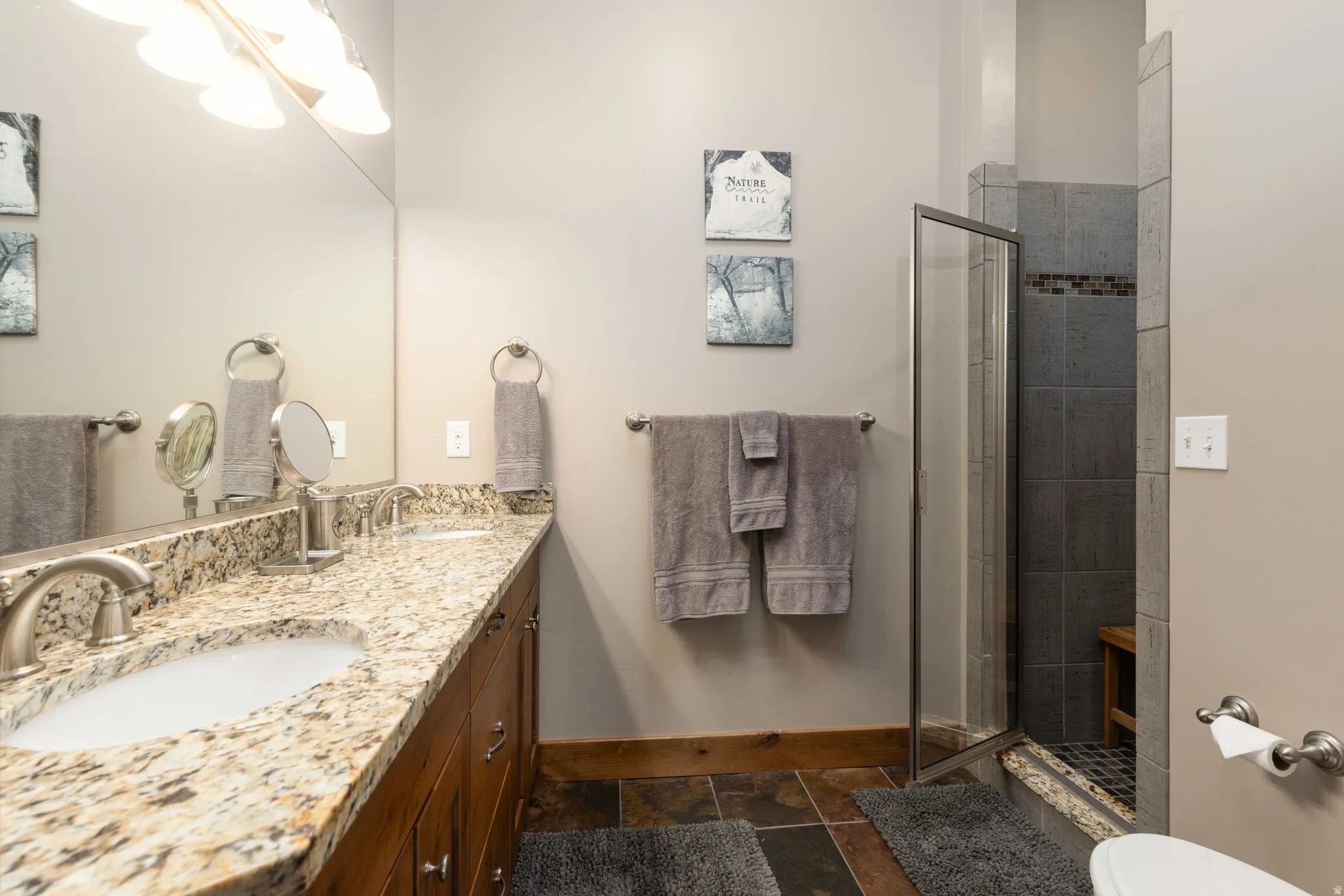 Full bath featuring double vanity, a shower stall, and stone tile floors