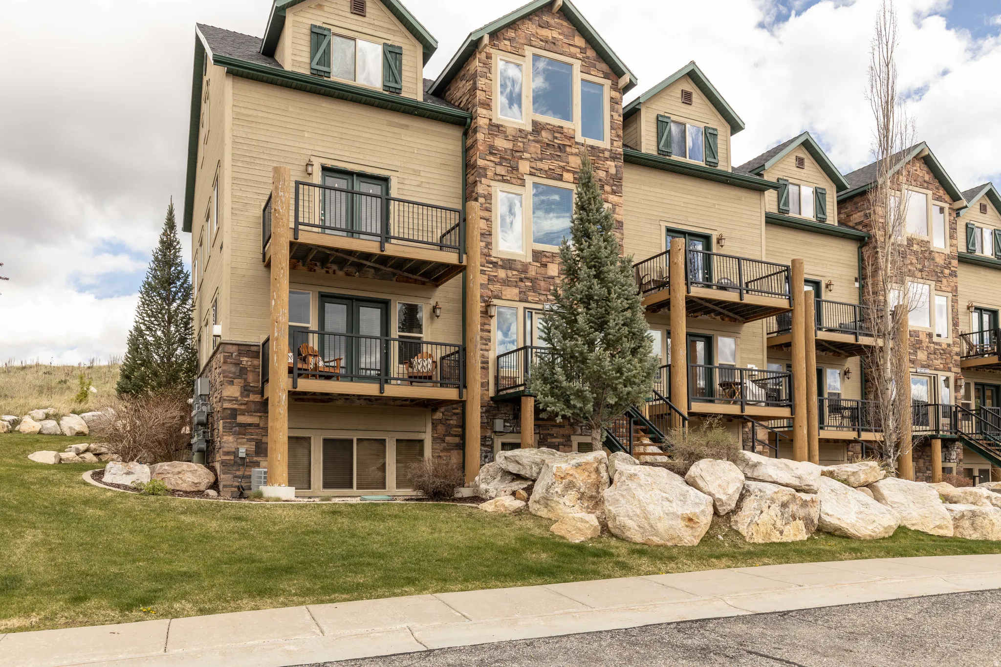 Rear view of property featuring stone siding, a balcony, a yard, and french doors