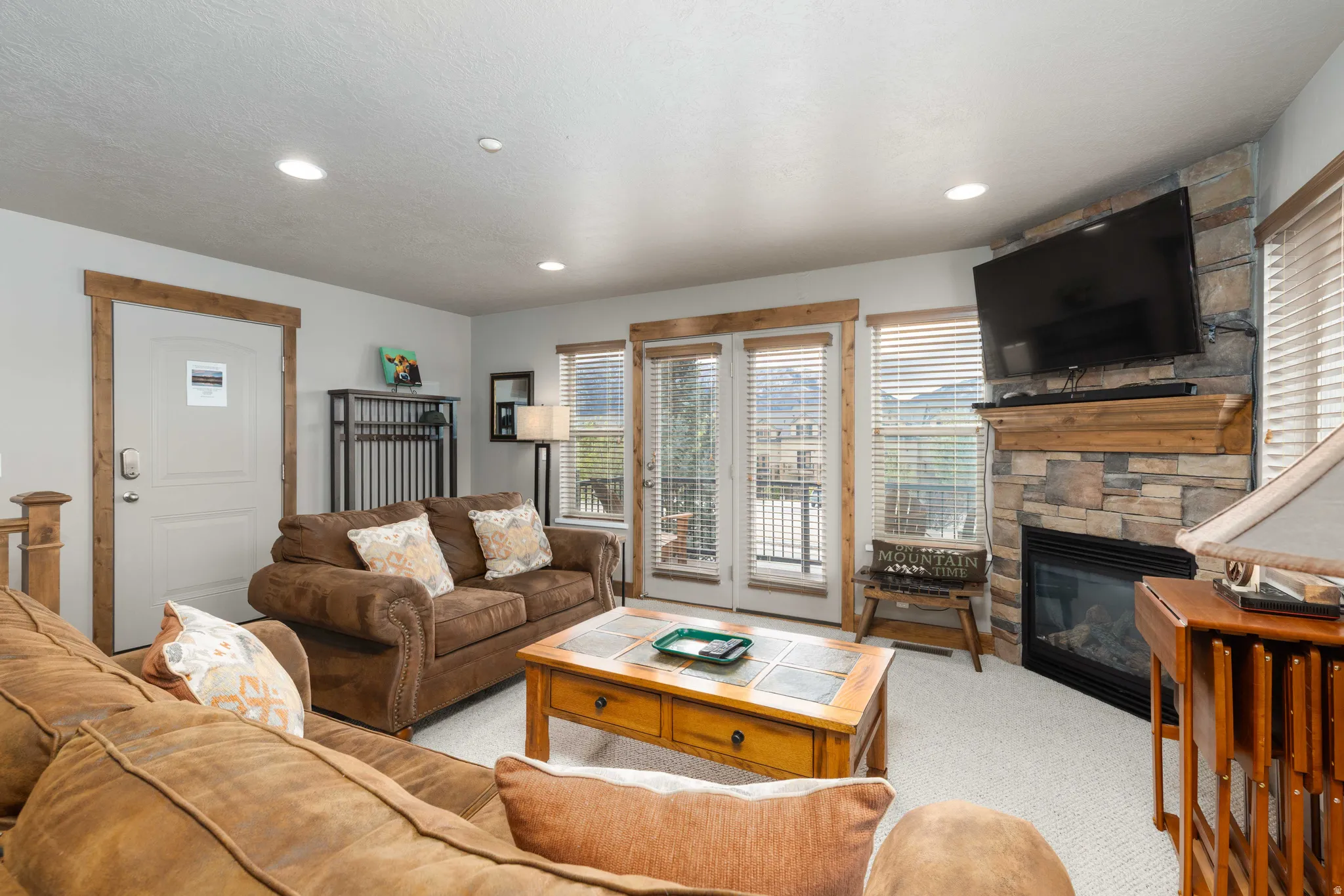 Carpeted living room featuring a stone fireplace and recessed lighting