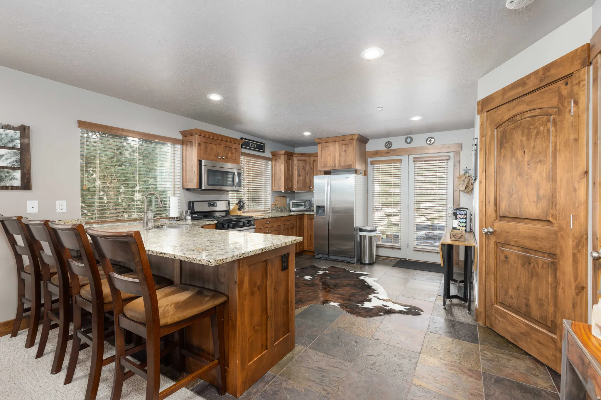 Kitchen featuring a peninsula, stone tile floors, wood finish cabinetry, stainless steel appliances, and light stone countertops
