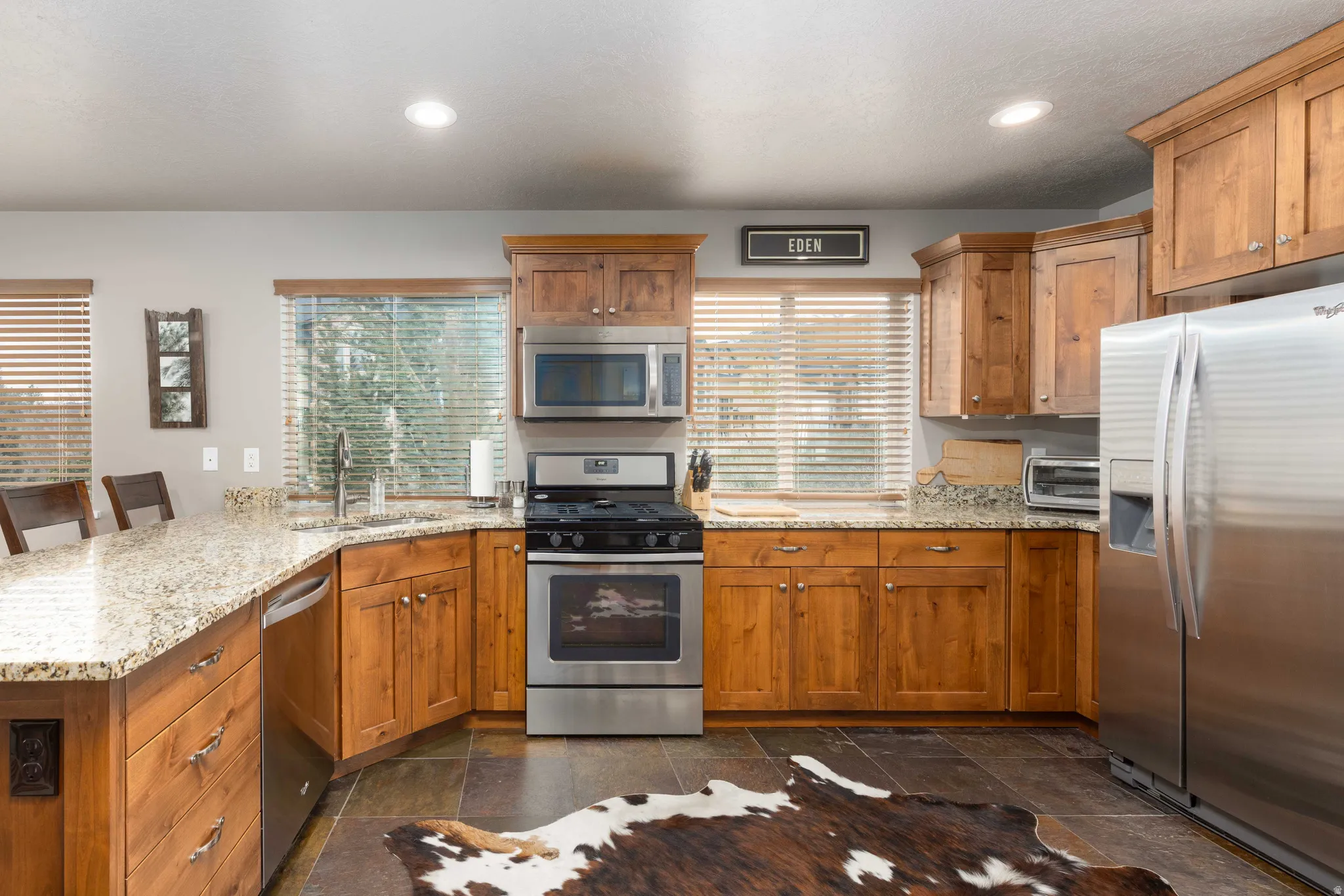 Kitchen featuring a peninsula, stainless steel appliances, light stone counters, a breakfast bar, and wood finish cabinets