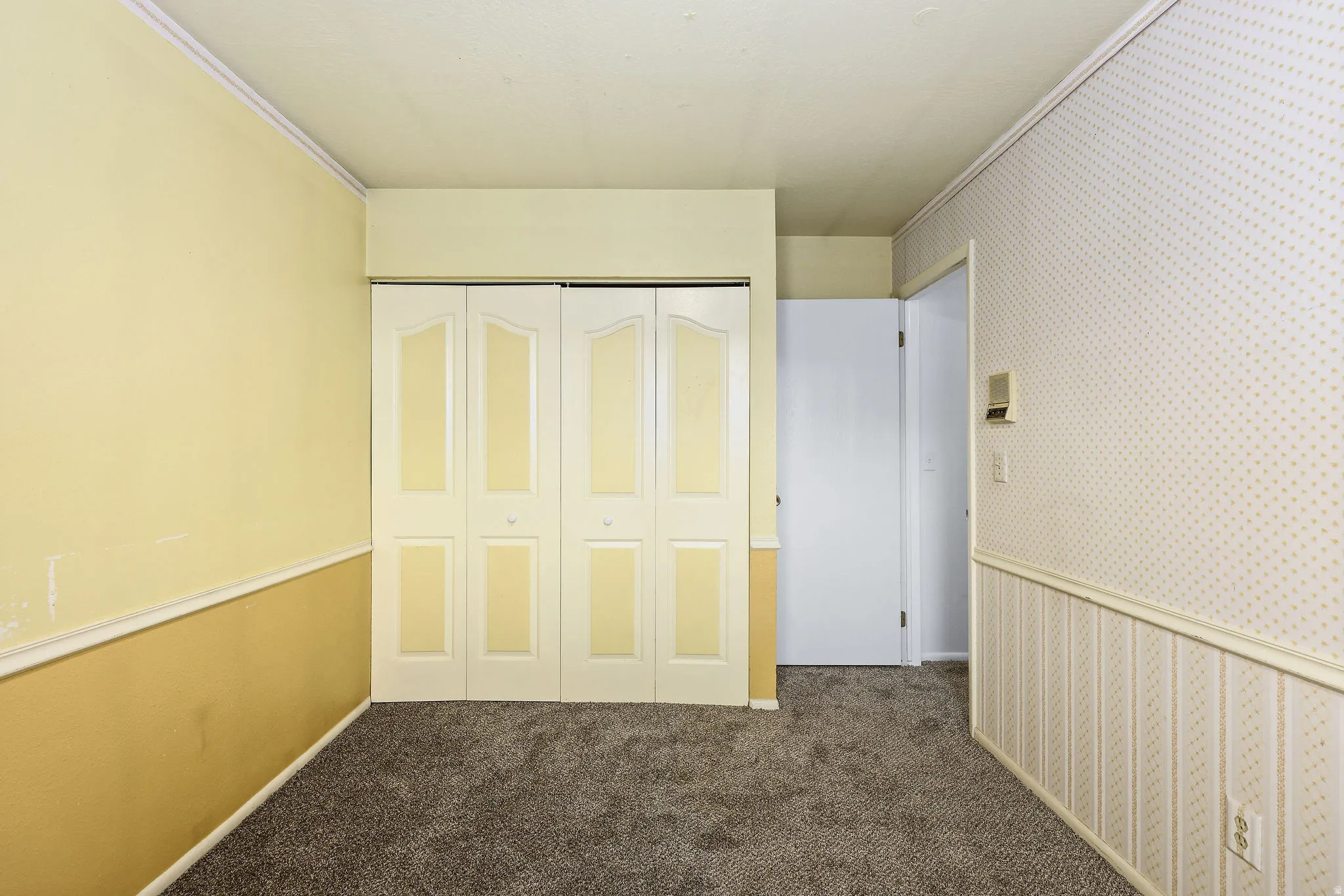 Unfurnished bedroom with wallpapered walls, dark carpet, and a closet