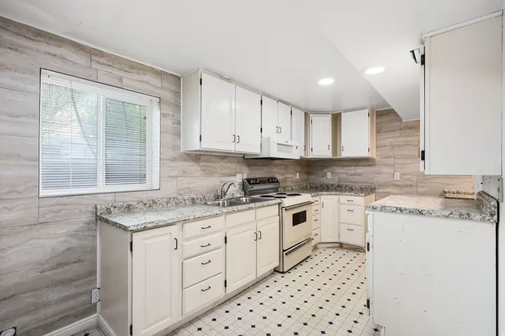 Kitchen featuring light countertops, white appliances, white cabinets, and light flooring