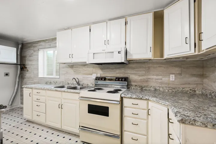 Kitchen featuring white appliances, backsplash, and white cabinetry