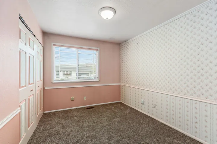 Unfurnished bedroom with wallpapered walls, a closet, dark carpet, and ornamental molding