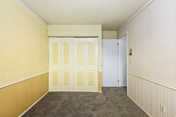 Unfurnished bedroom with wallpapered walls, dark carpet, and a closet