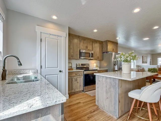 Kitchen with light stone countertops, a breakfast bar area, stainless steel appliances, light wood-type flooring, and recessed lighting