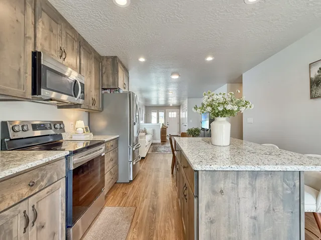 Kitchen with stainless steel appliances, light stone counters, a center island, a textured ceiling, and light wood-style floors