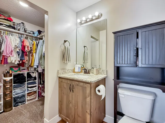 Bathroom featuring vanity, a walk in closet, a textured ceiling, and carpet