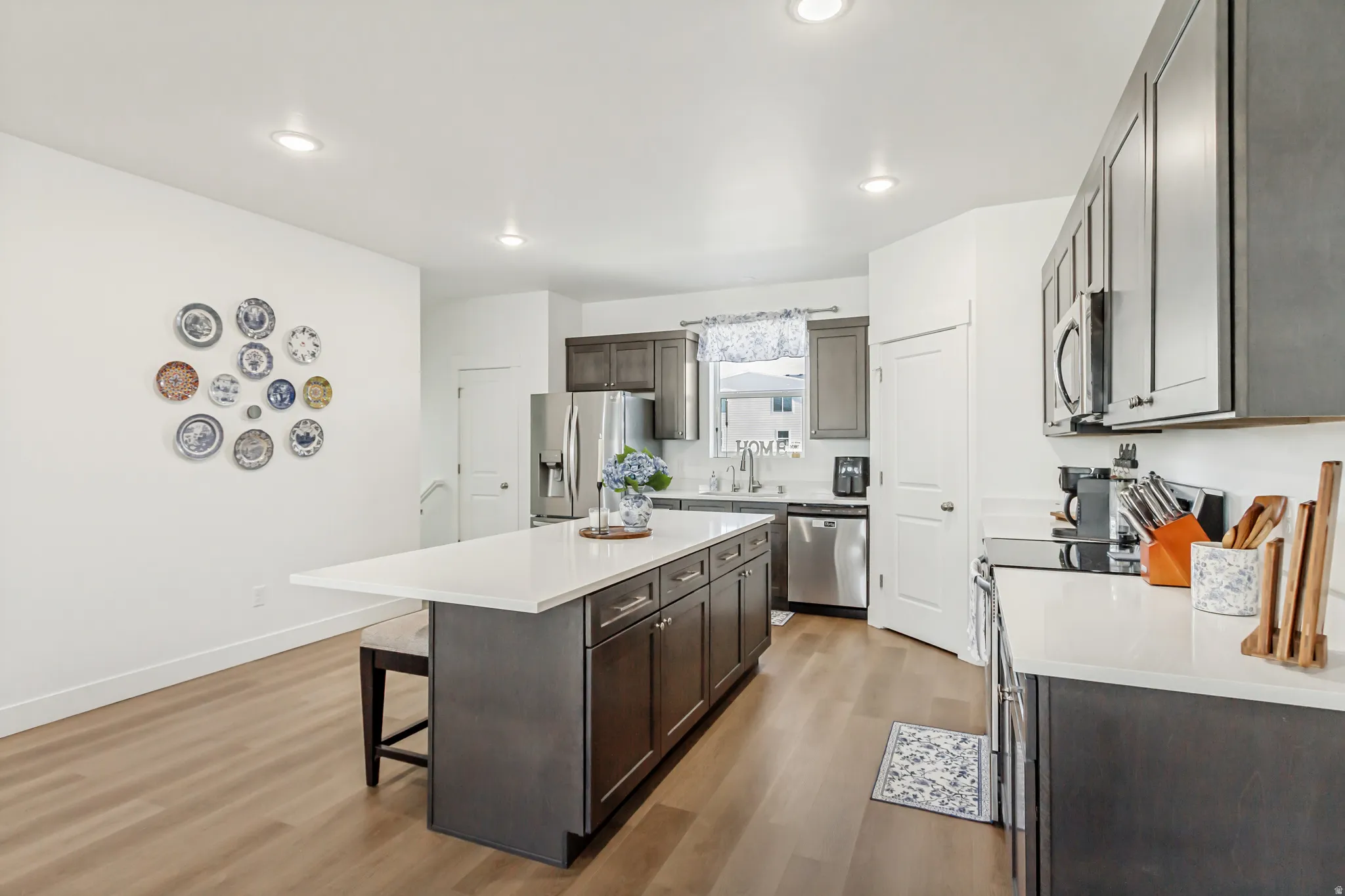 Kitchen featuring stainless steel appliances, light wood-type flooring, a kitchen bar, dark wood finish cabinets, and recessed lighting.