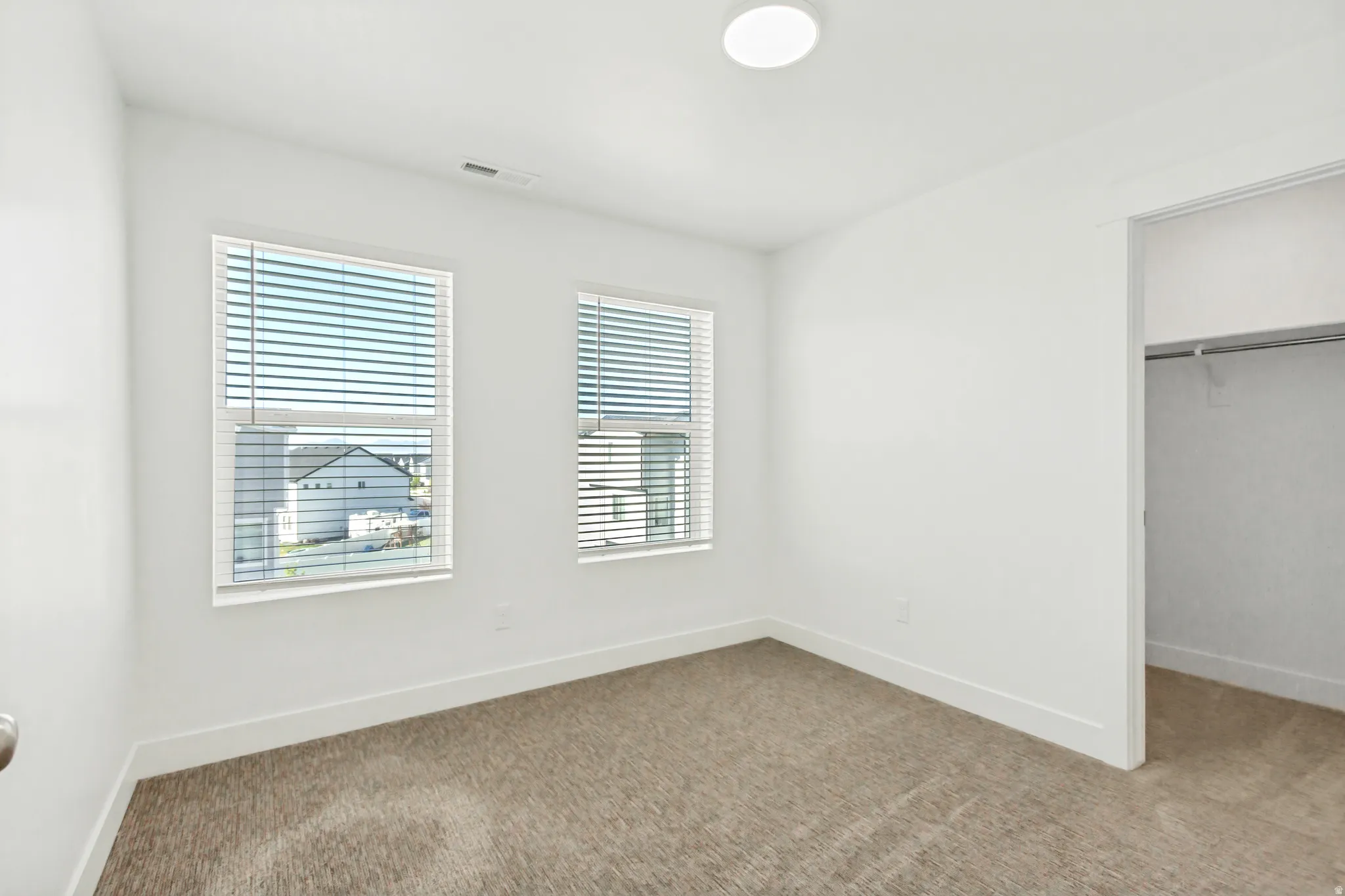Large bedroom featuring a walk in closet, light colored carpet and lots of natural light.