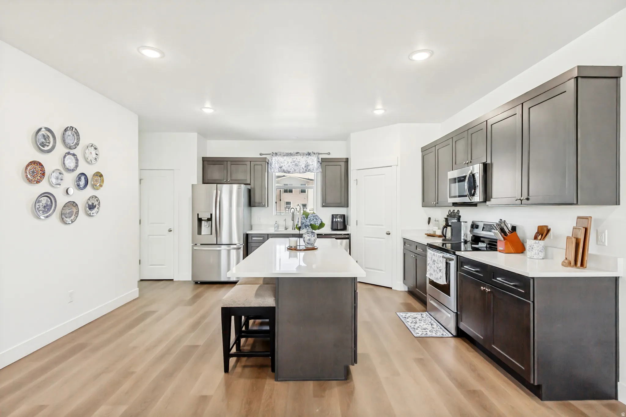 Kitchen featuring stainless steel appliances, light wood finished floors, a breakfast bar area, light stone counters, and a center island.