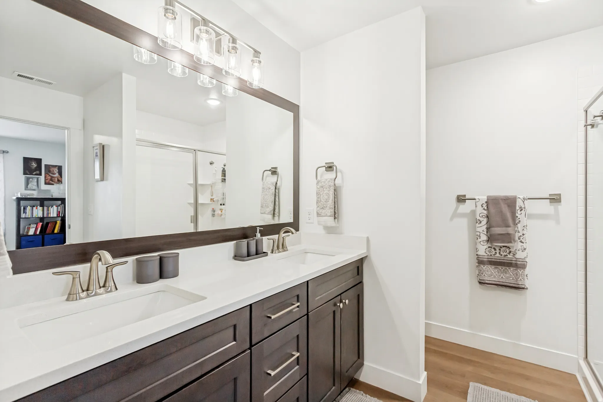 Large owners bathroom featuring double vanity, a shower stall, and light wood-style floors.