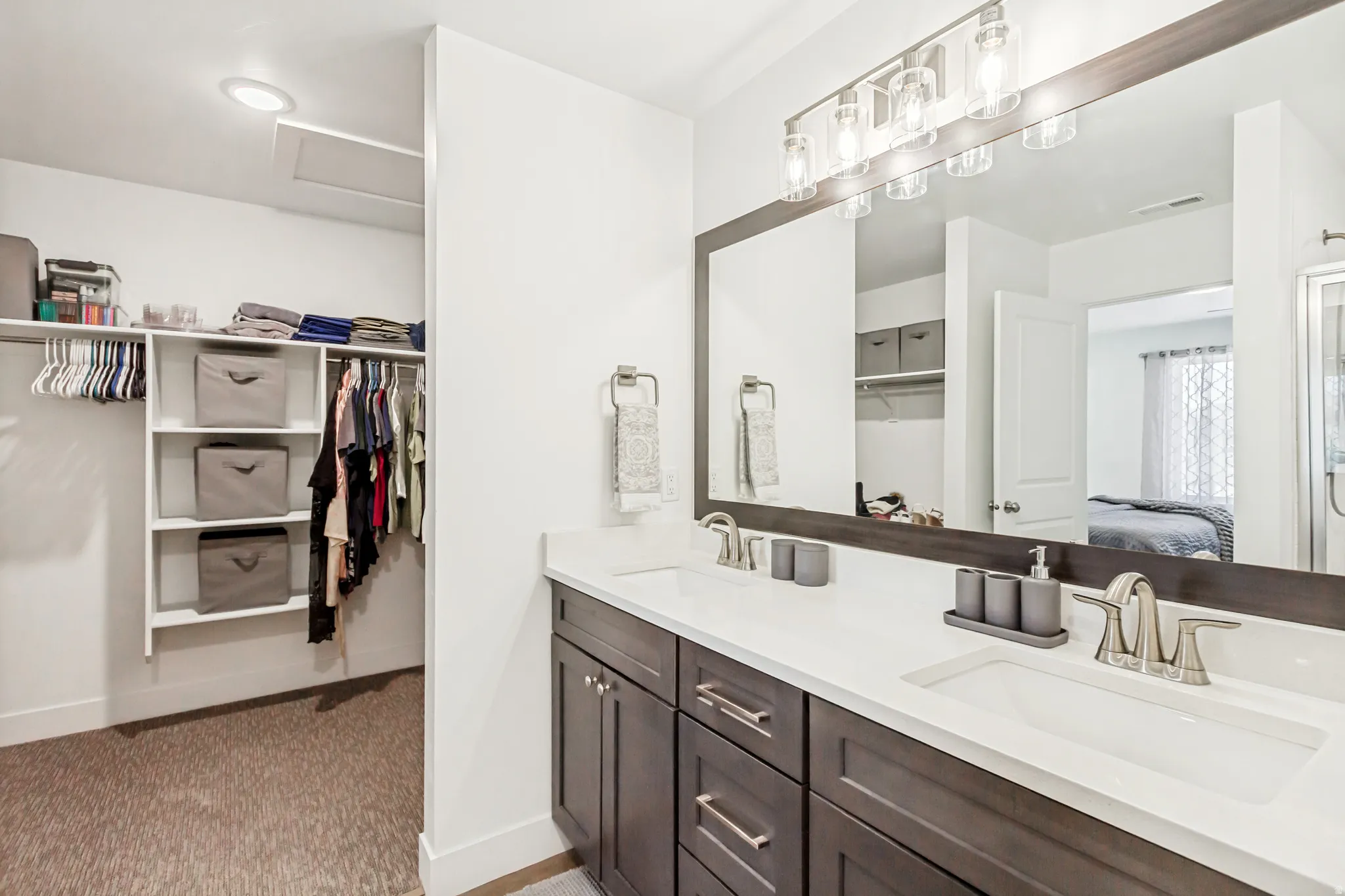 Ensuite bathroom with a walk in closet, double vanity, and light colored carpet