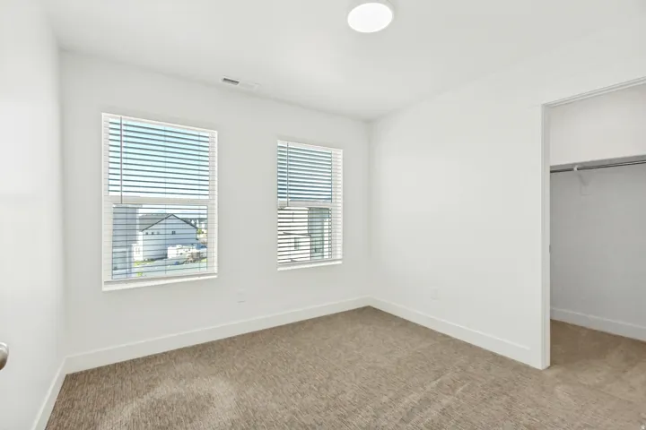 Large bedroom featuring a walk in closet, light colored carpet and lots of natural light.