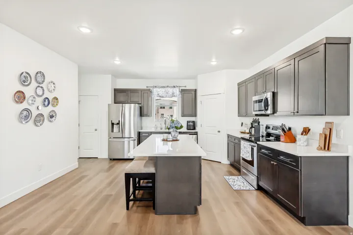 Kitchen featuring stainless steel appliances, light wood finished floors, a breakfast bar area, light stone counters, and a center island.