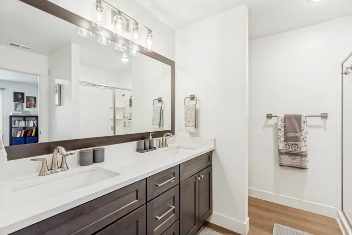 Large owners bathroom featuring double vanity, a shower stall, and light wood-style floors.