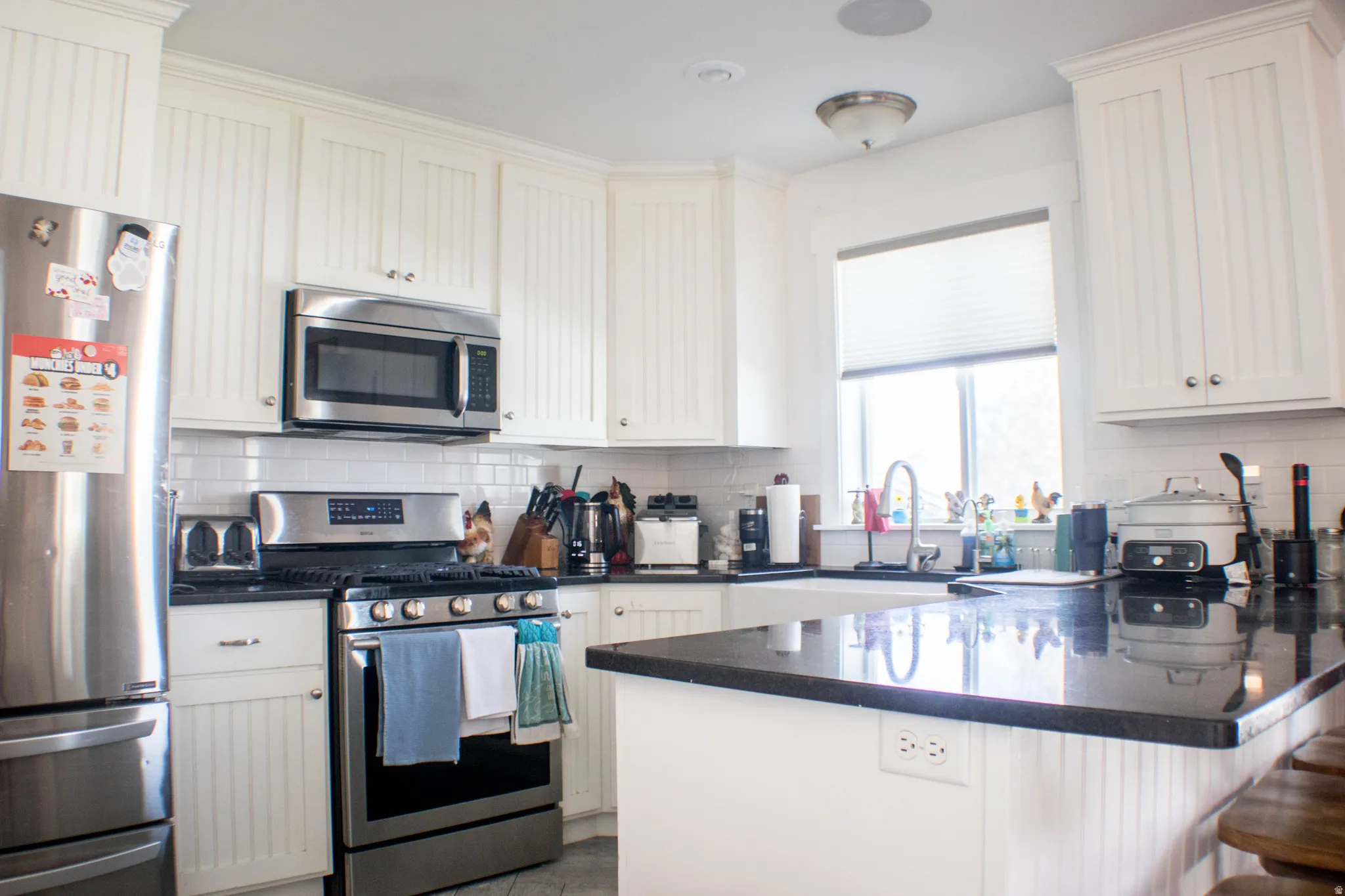 Kitchen with stainless steel appliances, a peninsula, dark stone counters, a kitchen bar, and tasteful backsplash