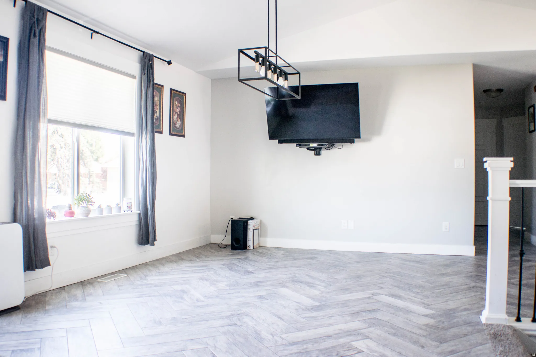 Spacious room featuring herringbone wood-finish flooring, a large window, vaulted ceilings, and a contemporary linear chandelier