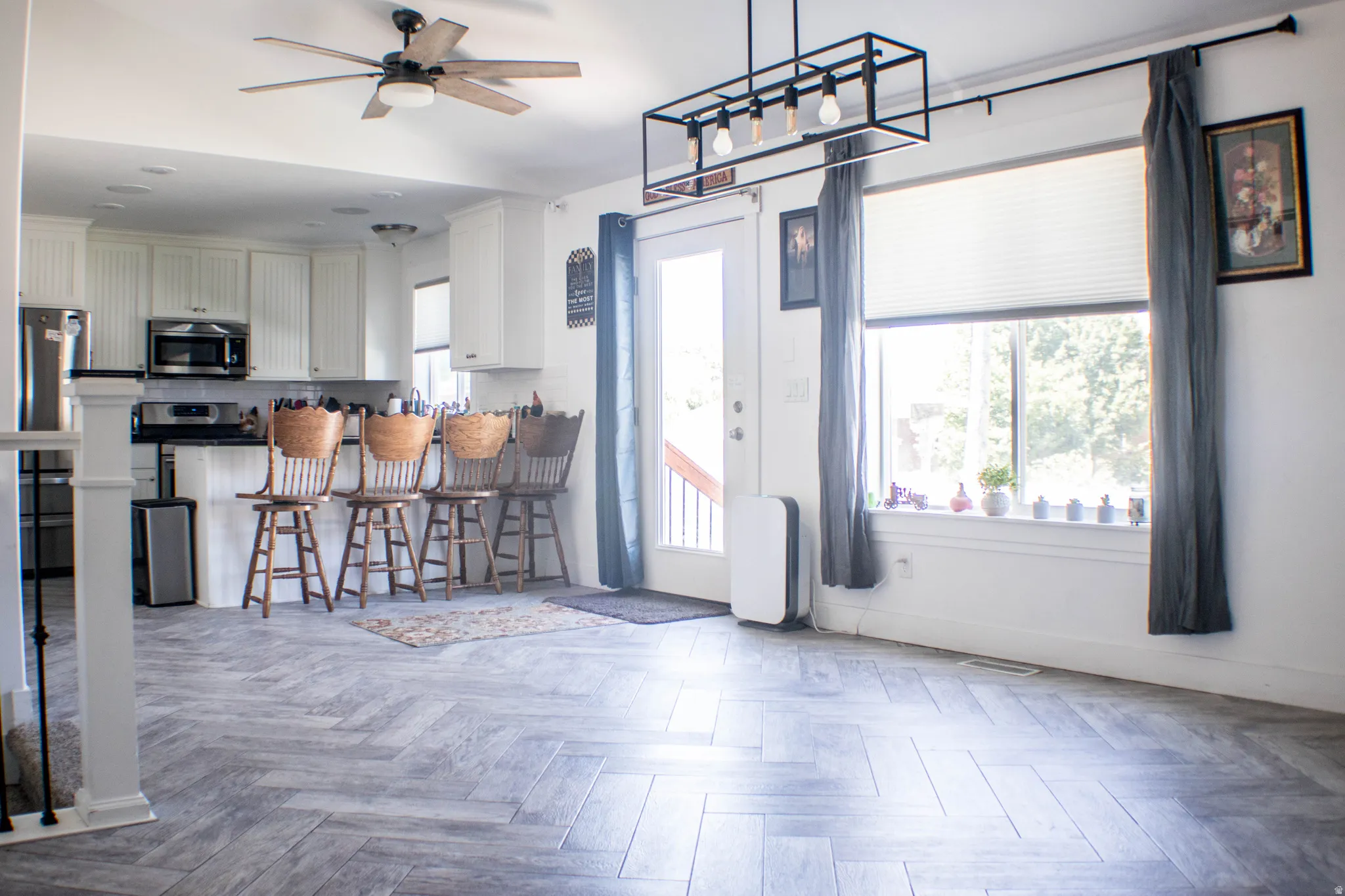 Open-concept living area featuring herringbone wood-finish flooring, white shaker-style cabinetry, stainless steel appliances, and a modern linear chandelier