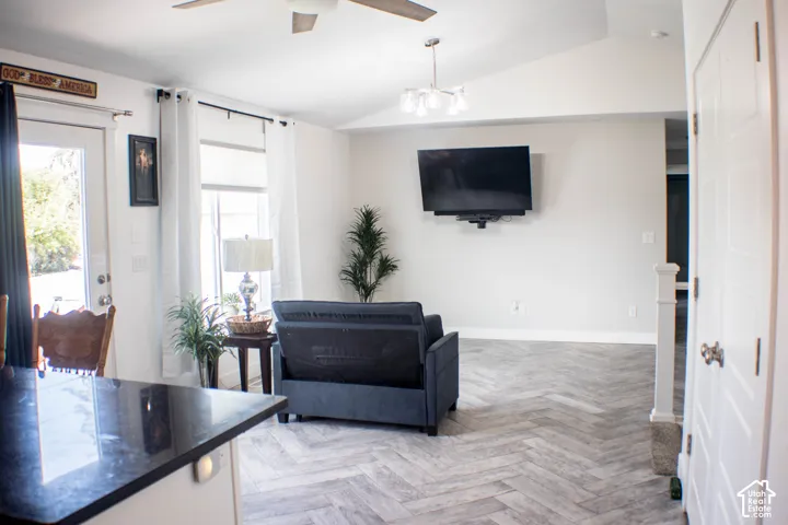 Spacious living area featuring a vaulted ceiling with a ceiling fan, herringbone-patterned wood-finish flooring, and white paneled interior doors