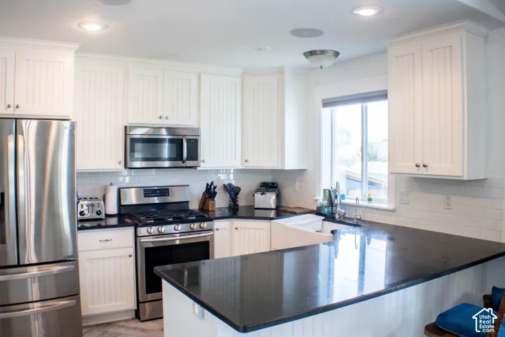 White shaker-style cabinetry with beadboard accents, stainless steel appliances, dark stone countertops, white subway tile backsplash, and an integrated farmhouse sink