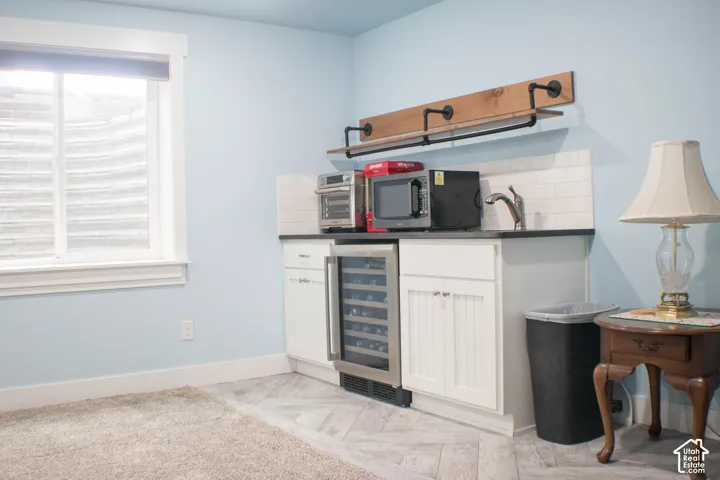 Built-in wet bar with white cabinetry, dark countertop, subway tile backsplash, and stainless steel beverage refrigerator