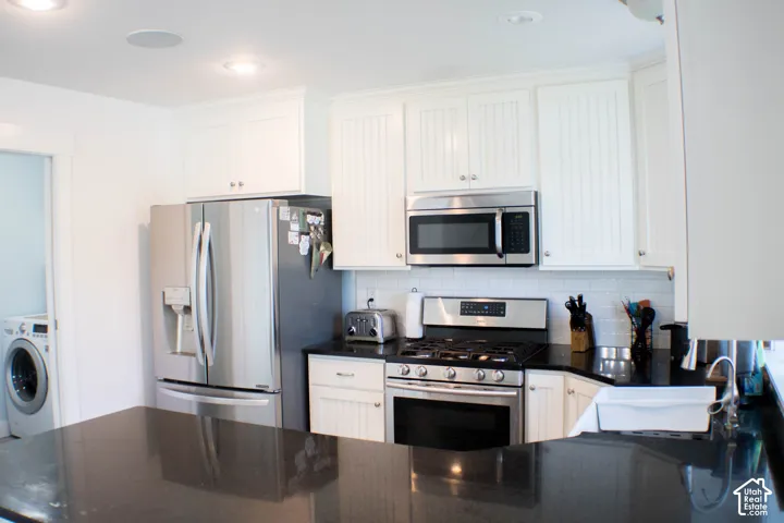 Kitchen featuring white cabinetry, dark countertops, stainless steel appliances, and a tile backsplash