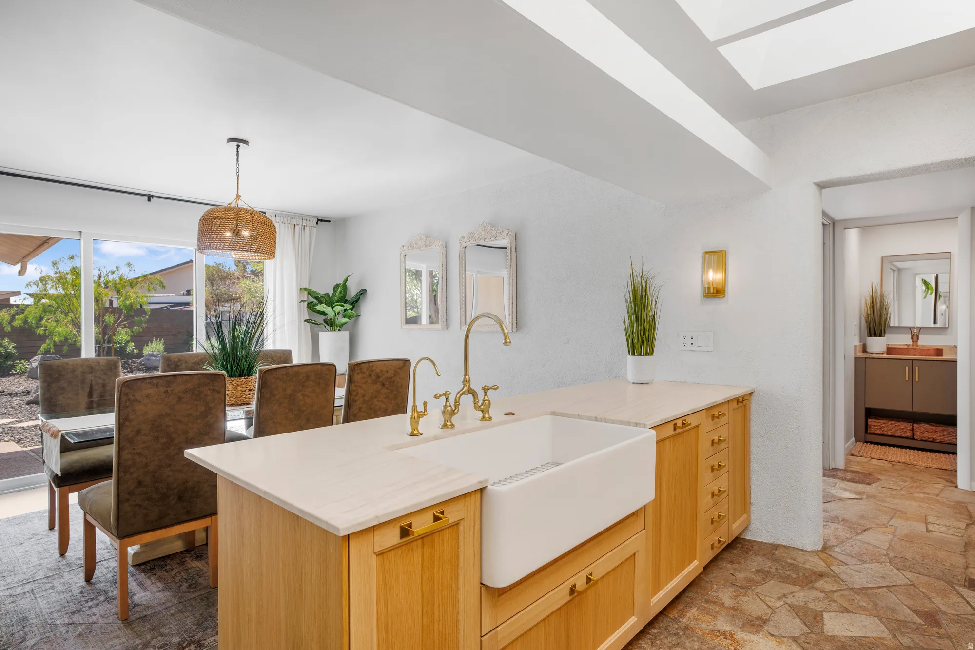 Kitchen with light wood finish cabinets, dark stone finish floors, hanging light fixtures, a peninsula, and light stone countertops