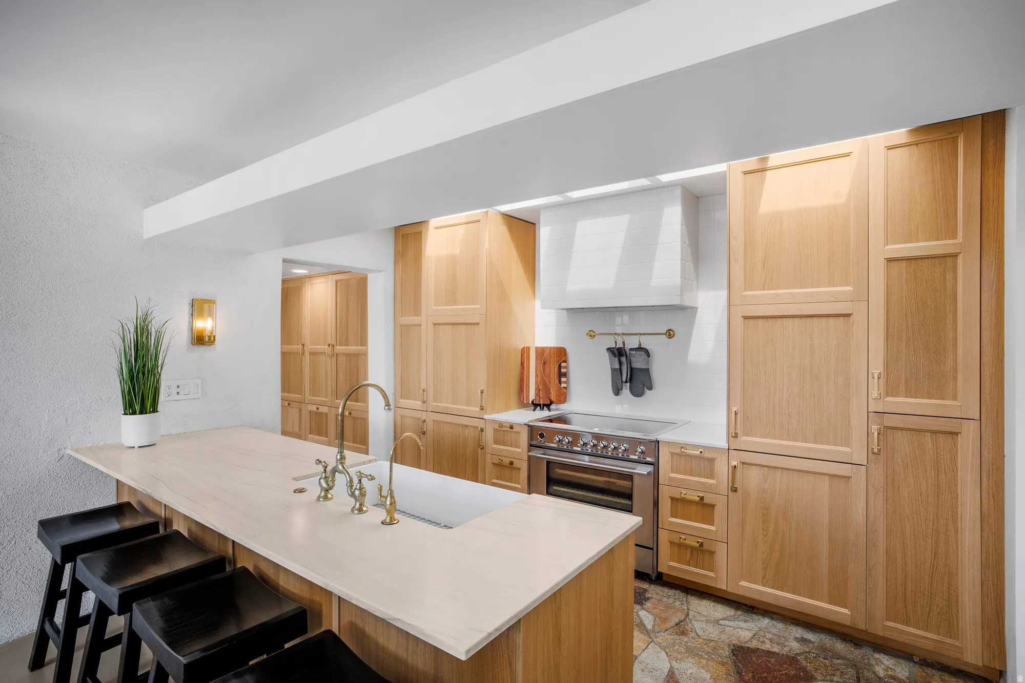 Kitchen featuring a breakfast bar area, a peninsula, light wood finish cabinets, stainless steel range with electric stovetop, and a textured wall