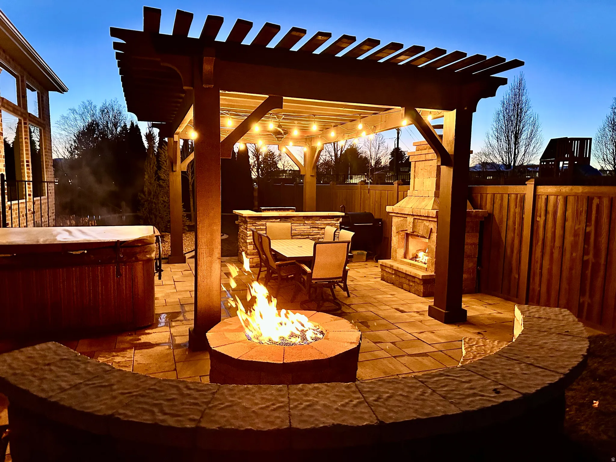 Patio terrace at dusk featuring a patio area, a hot tub, BBQ, a fire pit, and a pergola