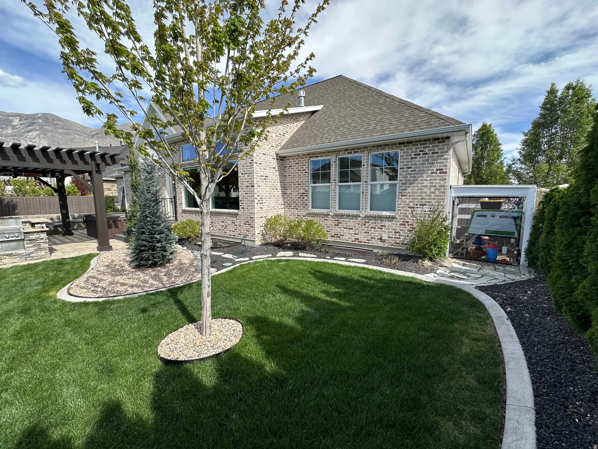 Back of property featuring a pergola, brick siding, a patio, roof with shingles, and an outdoor kitchen