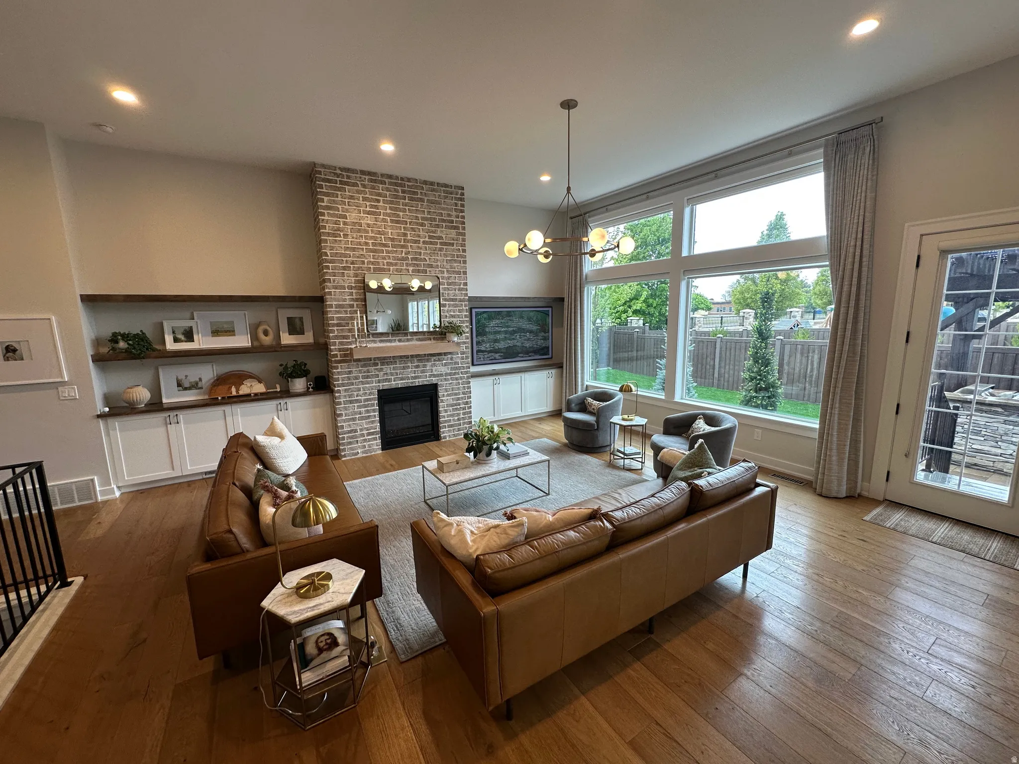Living room with hardwood / wood-style floors, hanging lights, and a brick fireplace