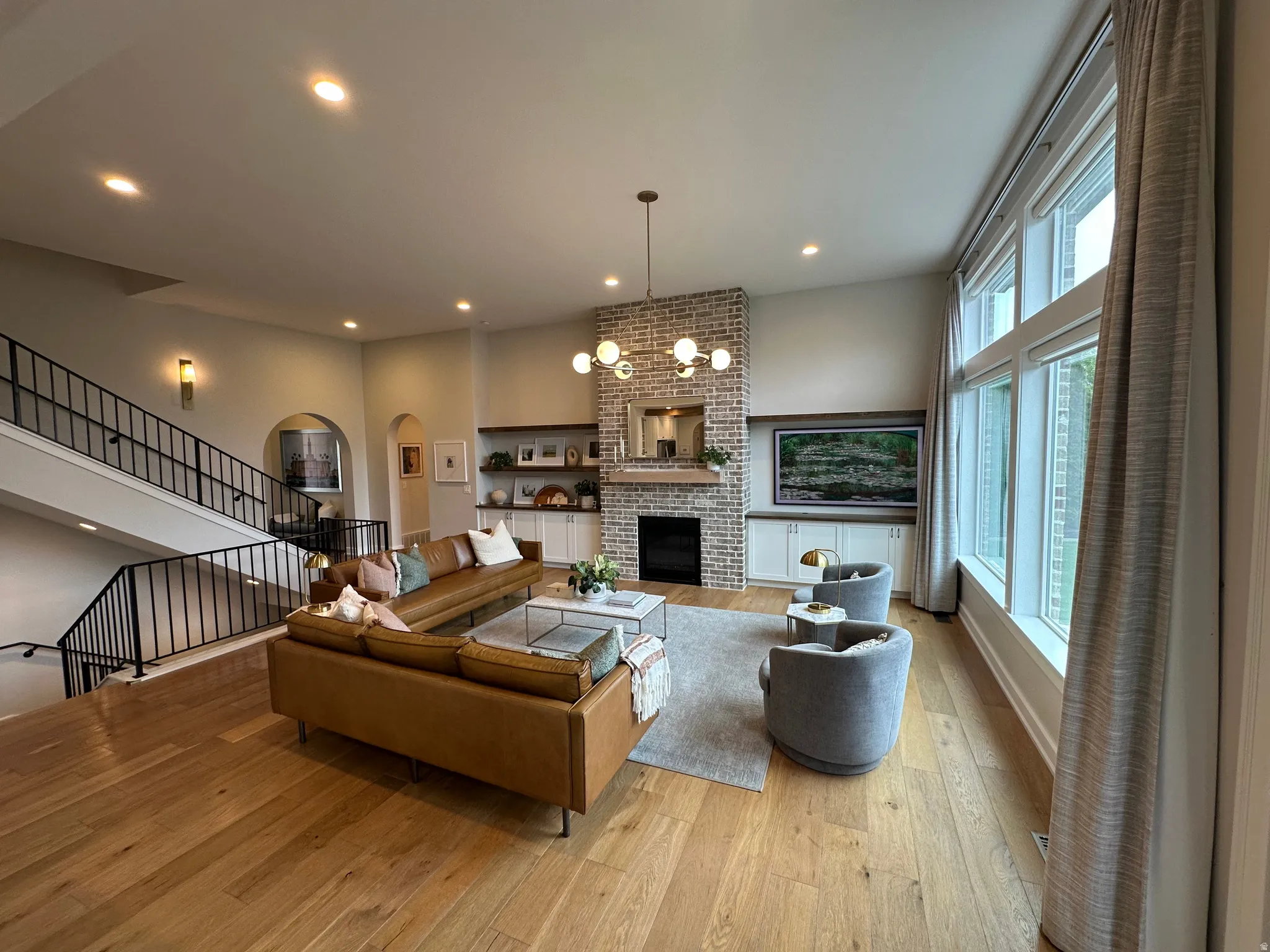 Living room featuring a chandelier, a brick fireplace, light wood finished floors, arched walkways, and a high ceiling