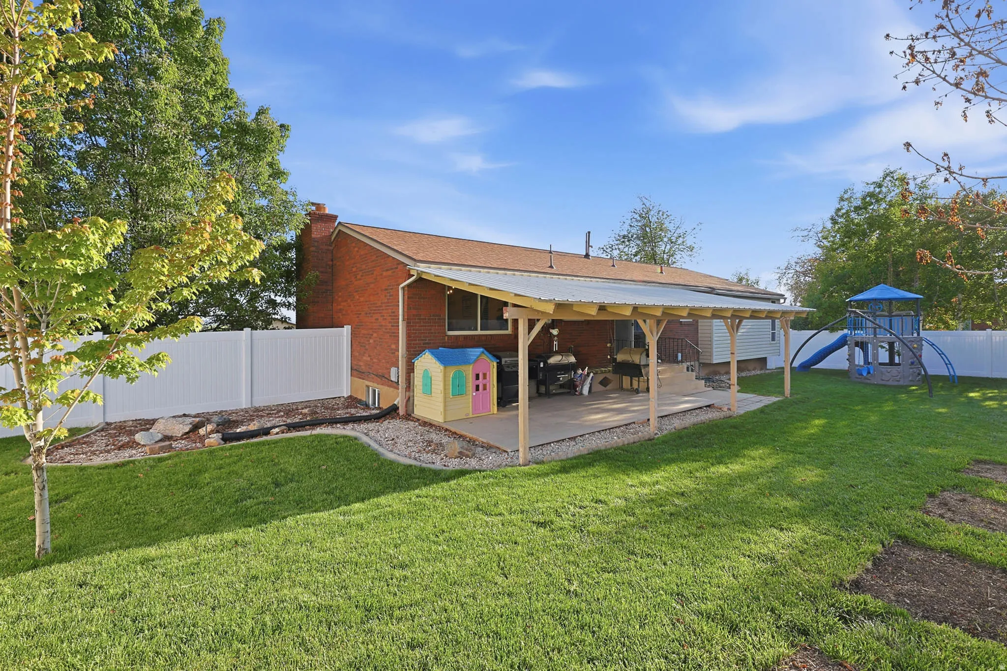 Back of house featuring a fenced backyard, a chimney, brick siding, a playground, and a patio