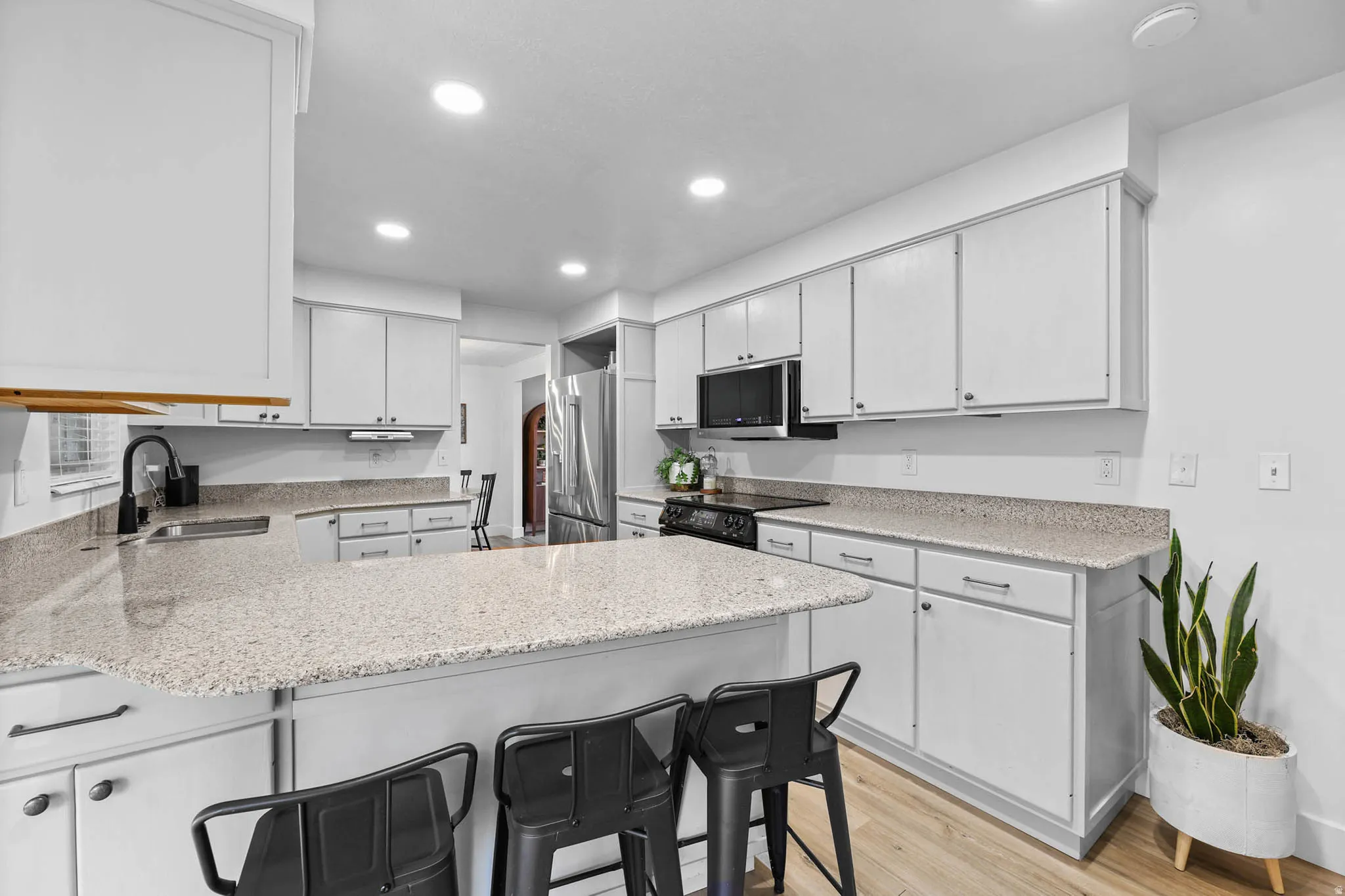 Kitchen featuring a kitchen breakfast bar, a peninsula, light wood-type flooring, high quality fridge, and light stone countertops