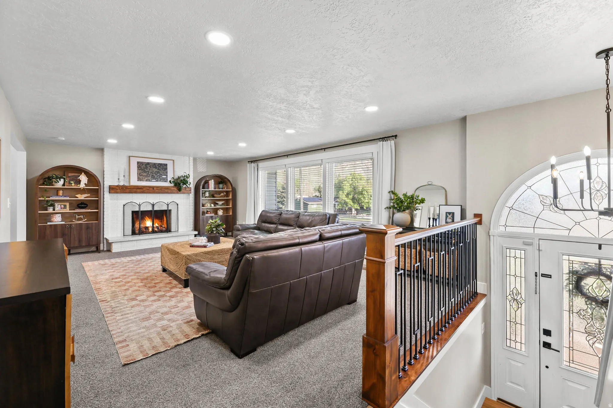 Carpeted living area featuring a textured ceiling, hanging lights, a brick fireplace, and built in shelves
