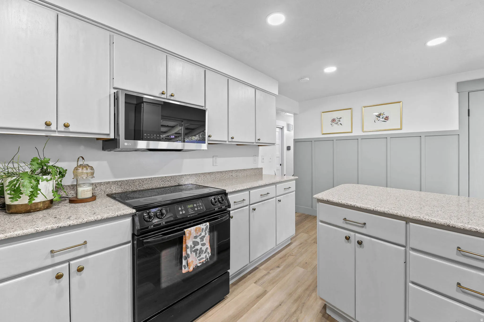Kitchen featuring electric range, a decorative wall, light wood-style flooring, stainless steel microwave, and wainscoting