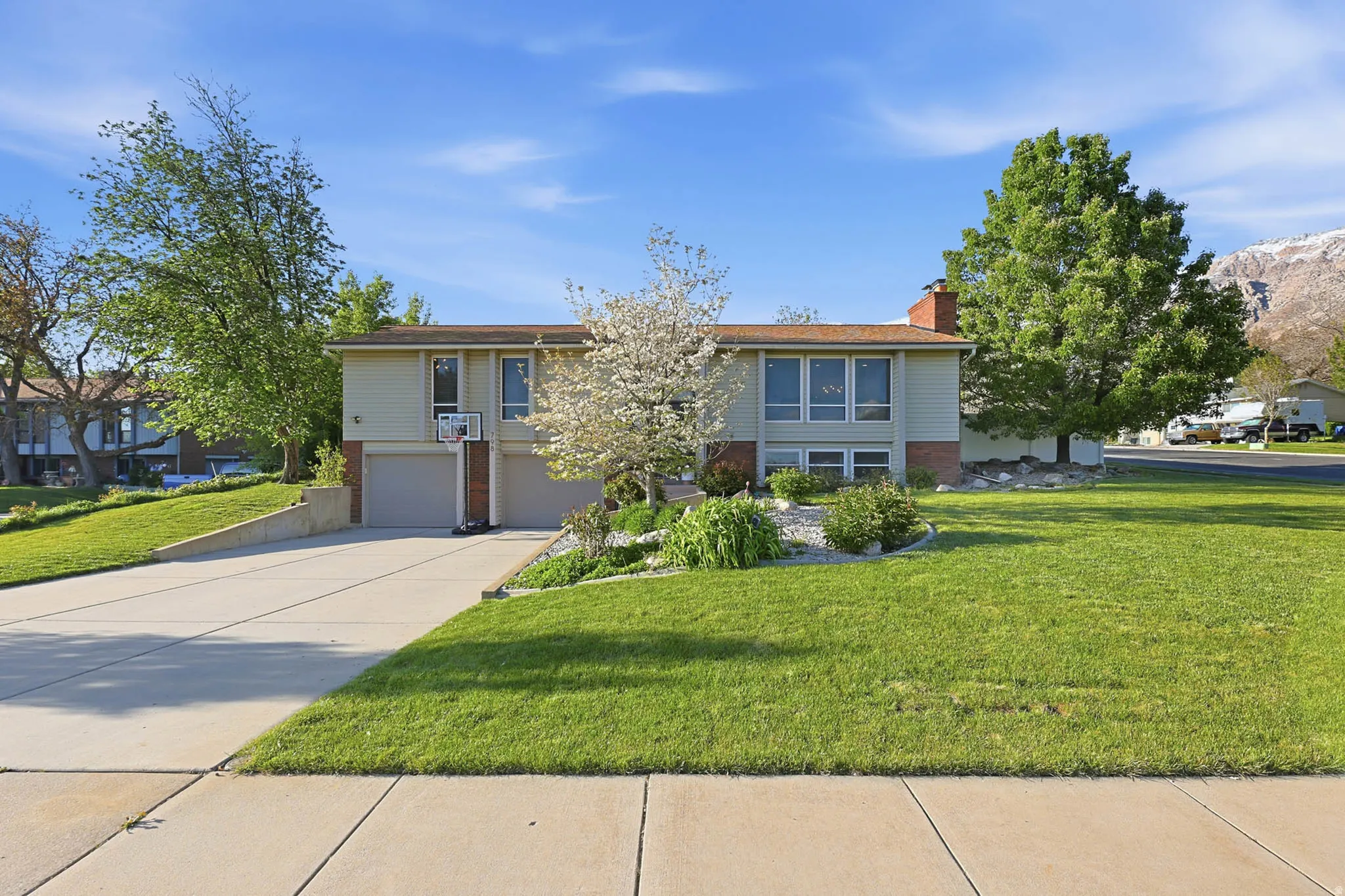 Raised ranch with brick siding, a front lawn, concrete driveway, an attached garage, and a chimney