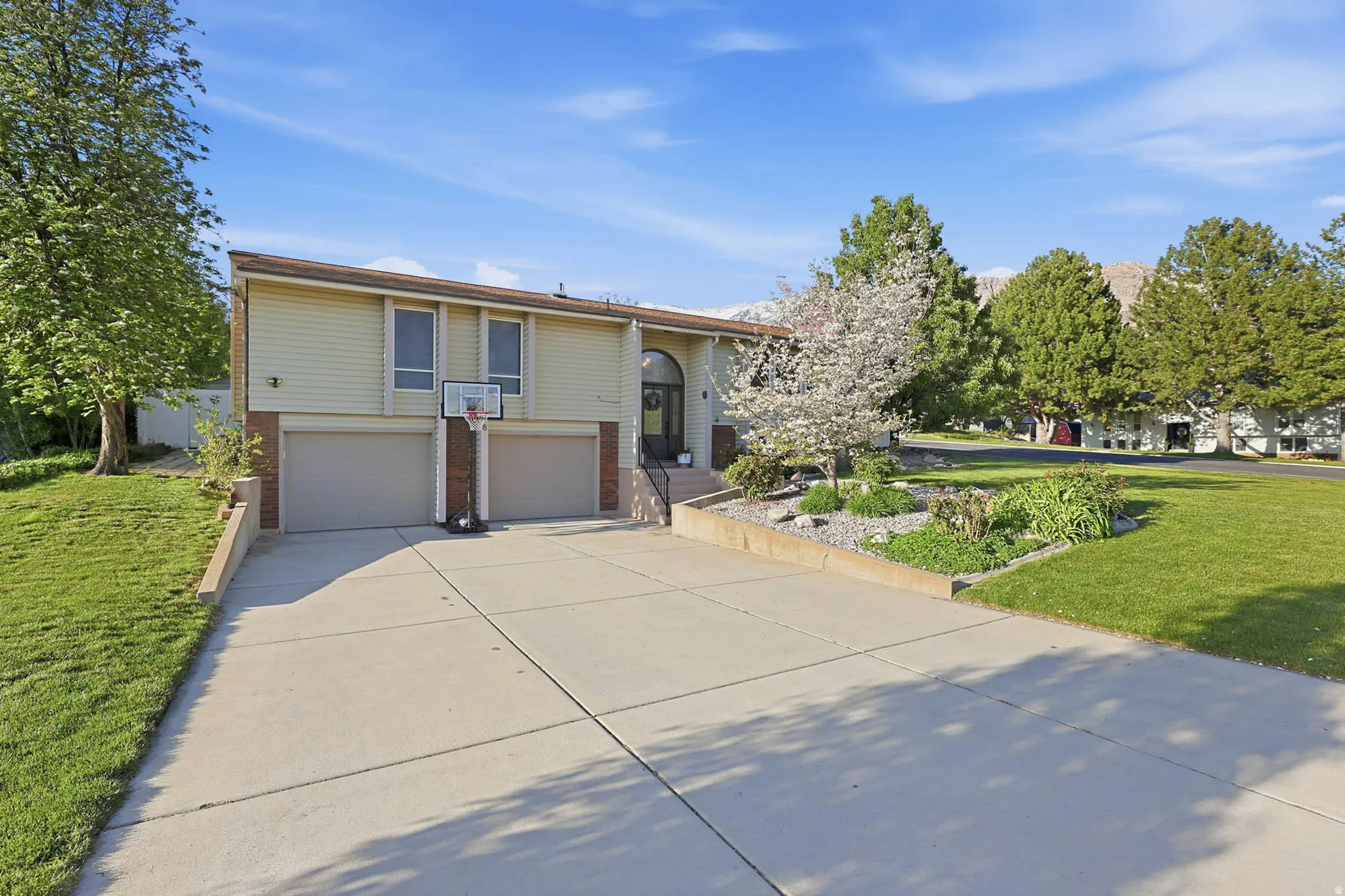 Raised ranch featuring a front yard, an attached garage, brick siding, and concrete driveway