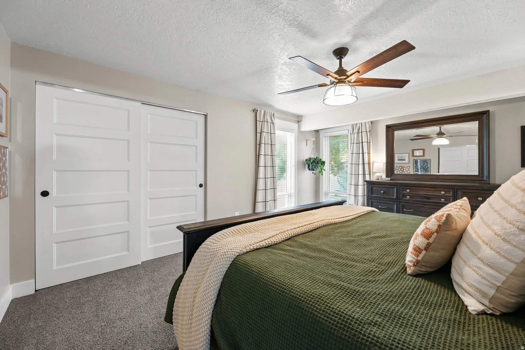 Bedroom with a textured ceiling, a closet, dark colored carpet, and a ceiling fan
