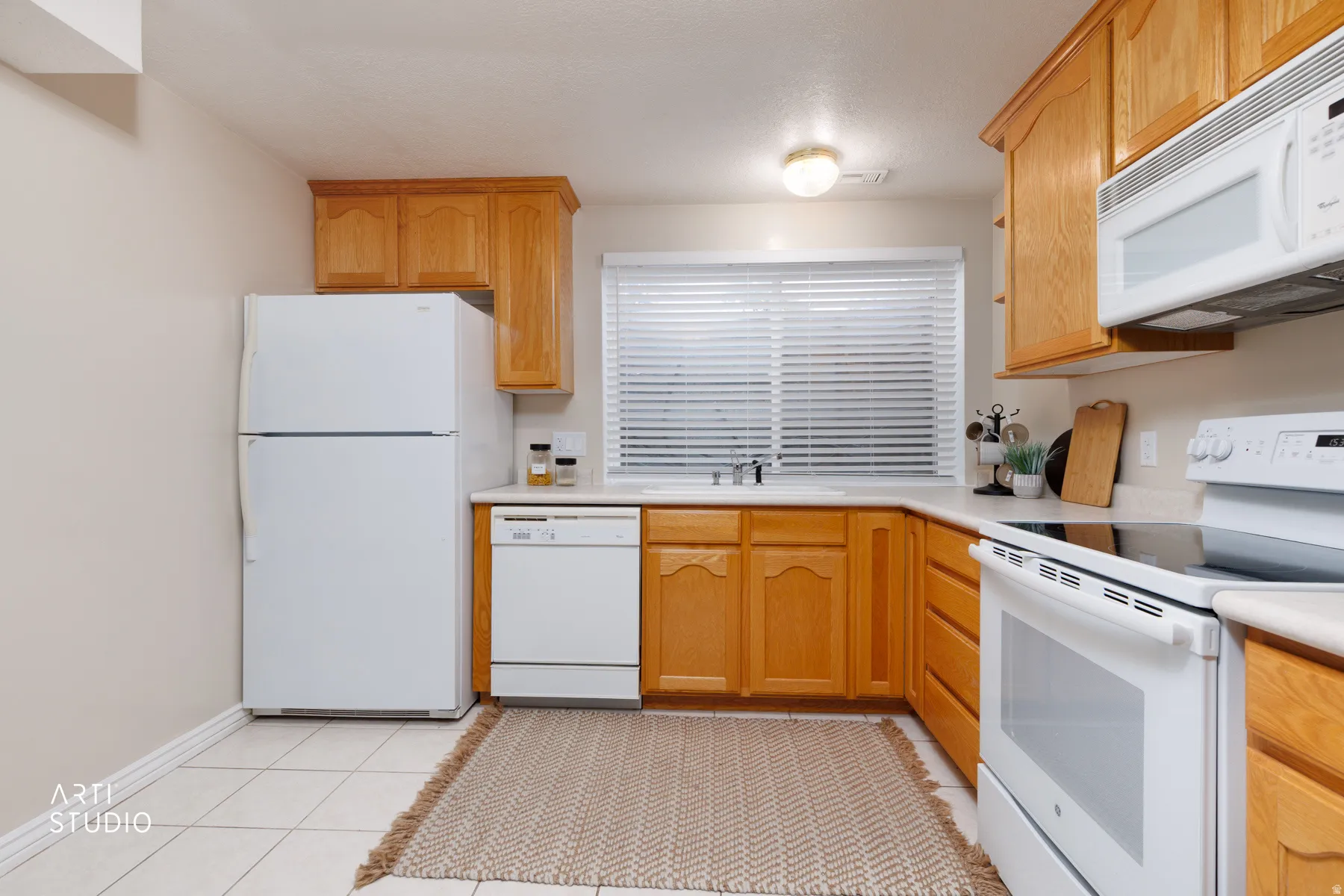 Kitchen with white appliances, light countertops, light tile patterned floors, and light wood finish cabinetry