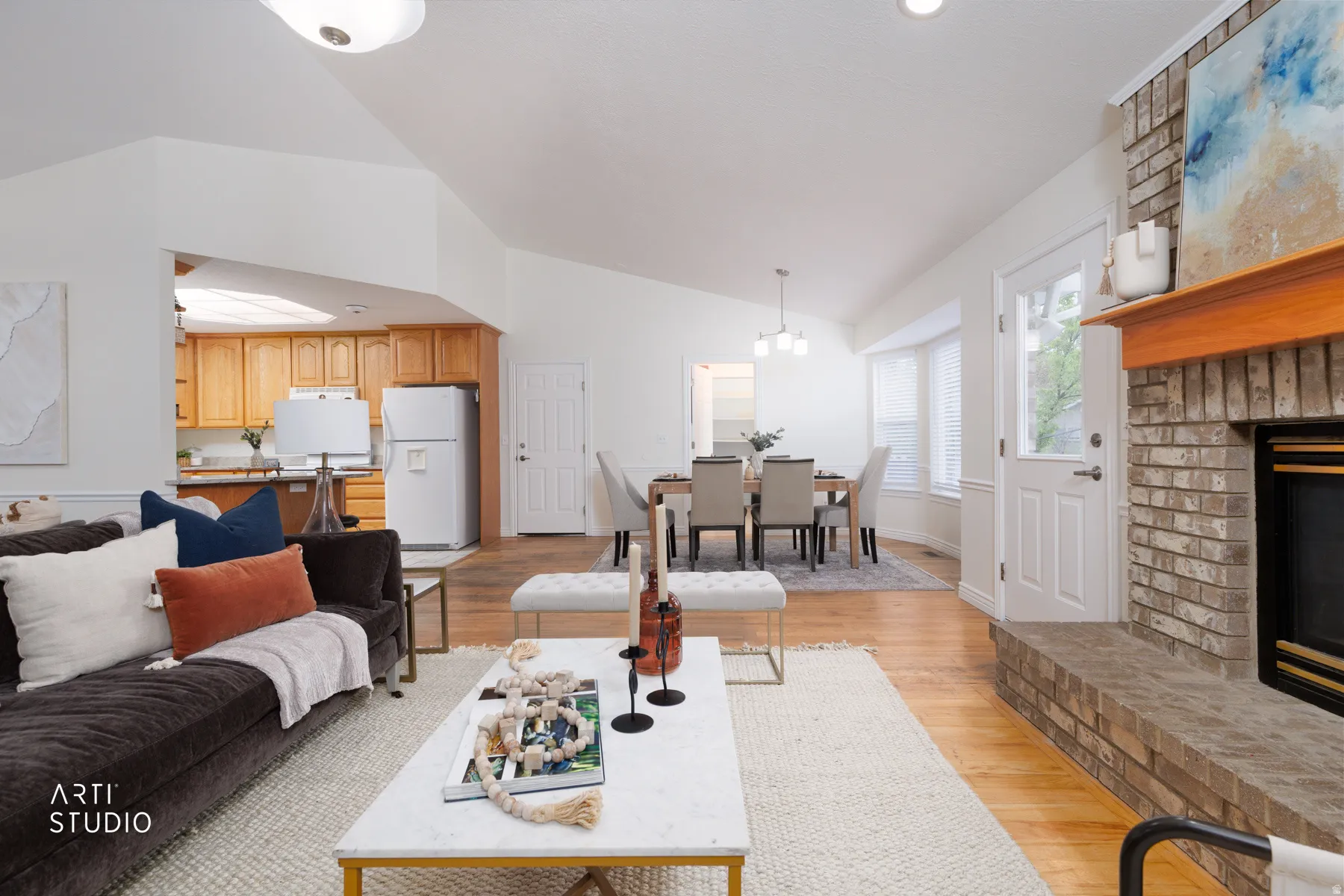 Living area with a brick fireplace, light wood-style floors, and lofted ceiling