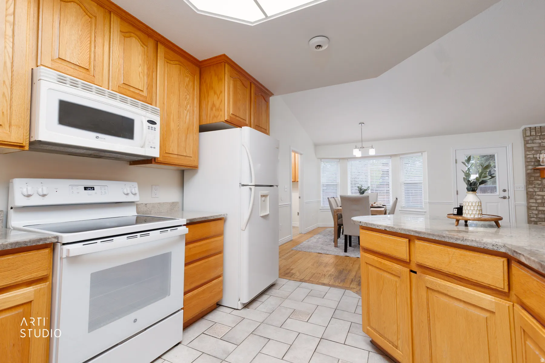 Kitchen with white appliances, light stone countertops, lofted ceiling, and pendant lighting