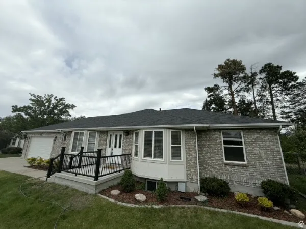 Brick exterior with a dark shingle roof, featuring a front entry deck with black railings, a bay window, and an attached garage with a white door