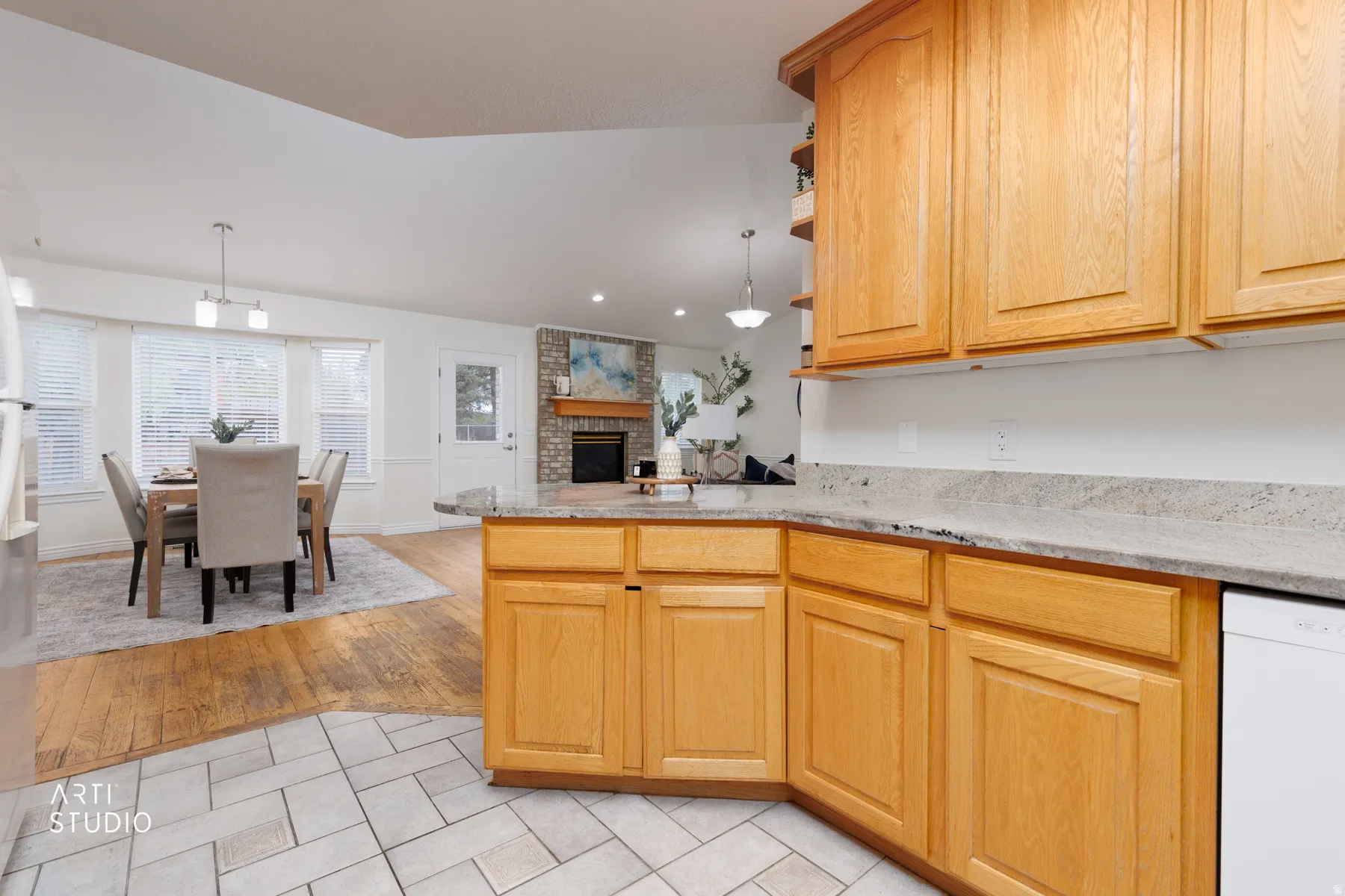 Kitchen featuring a peninsula, a brick fireplace, white dishwasher, light tile patterned floors, and light stone counters
