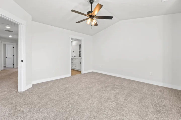 Unfurnished bedroom featuring light carpet, ensuite bath, ceiling fan, and lofted ceiling
