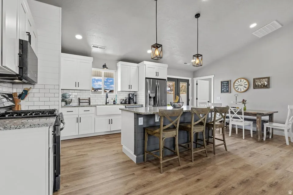 Kitchen with stainless steel appliances, light stone countertops, white cabinetry, a center island, and a kitchen bar