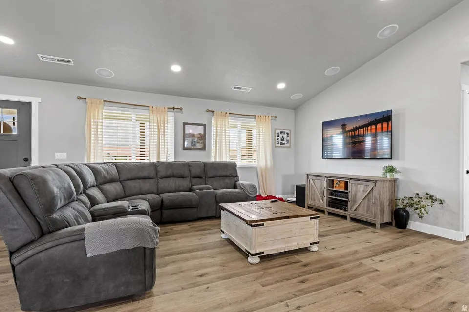 Living room with light wood finished floors, lofted ceiling, and recessed lighting